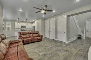 Living room with stairway, light wood-type flooring, a ceiling fan, and recessed lighting