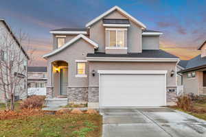 View of front facade with stone siding, stucco siding, concrete driveway, and a garage