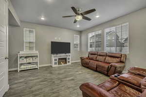 Living area with ceiling fan, wood finished floors, recessed lighting, healthy amount of natural light, and a warm lit fireplace