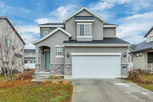 View of front of home with stone siding, stucco siding, concrete driveway, and a garage