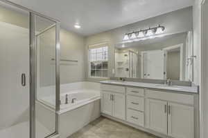 Bathroom featuring a stall shower, a garden tub, double vanity, and light tile patterned floors