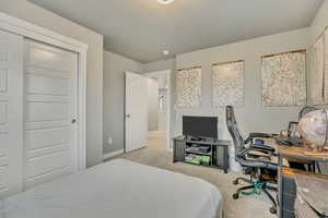 Bedroom featuring a closet, light carpet, a desk, and a textured ceiling