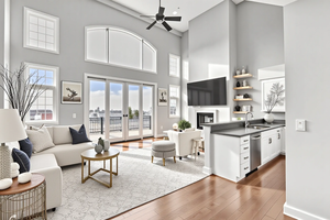 Family Room with a ceiling fan, a glass covered fireplace, dark wood-type flooring, plenty of natural light, and a high ceiling