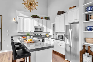 Kitchen featuring, stainless steel appliances, a towering ceiling, white cabinetry, and a kitchen breakfast bar