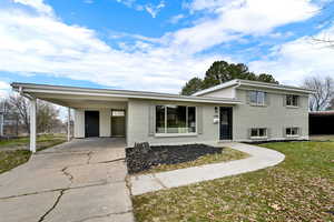 Split level home with an attached carport, brick siding, a front lawn, and driveway