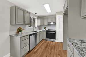 Kitchen with gray cabinets, stainless steel appliances, light stone countertops, pendant lighting, and under cabinet range hood