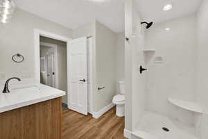 Full bath with vanity, a textured ceiling, a marble finish shower, and light wood-style flooring