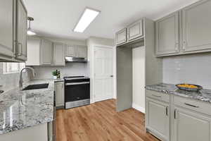 Kitchen featuring electric stove, light stone counters, gray cabinetry, backsplash, and under cabinet range hood