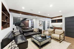 Living room featuring bar with sink, light wood-type flooring, beam ceiling, and recessed lighting