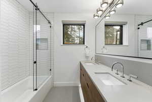 Full bathroom with double vanity, bath / shower combo with glass door, and light tile patterned floors