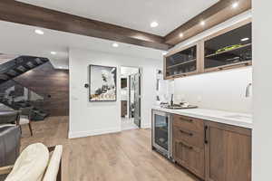 Indoor wet bar with stairway, glass insert cabinets, beverage cooler, light wood-type flooring, and brown cabinetry