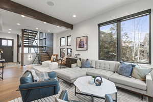 Living area with stairway, beam ceiling, healthy amount of natural light, recessed lighting, and wood finished floors