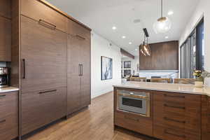 Kitchen with pendant lighting, recessed lighting, light wood finished floors, brown cabinetry, and light stone counters