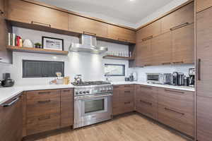 Kitchen with open shelves, high end range, wall chimney exhaust hood, tasteful backsplash, and modern cabinets