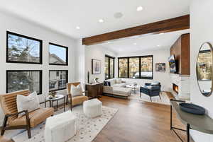 Living area with beamed ceiling, a lit fireplace, wood finished floors, and recessed lighting