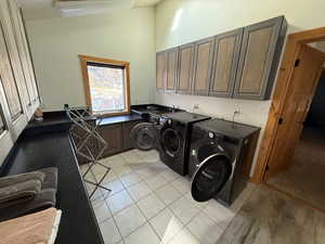 Washroom with independent washer and dryer, vaulted ceiling, cabinet space, and light tile patterned floors