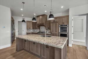 Kitchen with hanging light fixtures, light stone counters, a large island with sink, appliances with stainless steel finishes, and backsplash