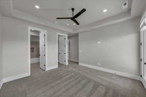 Unfurnished bedroom featuring a tray ceiling, light carpet, connected bathroom, ceiling fan, and recessed lighting