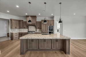 Kitchen featuring hanging light fixtures, light stone countertops, a large island, light wood-style floors, and decorative backsplash