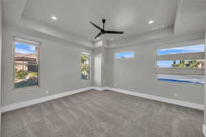 Empty room featuring a tray ceiling, light colored carpet, ceiling fan, and recessed lighting