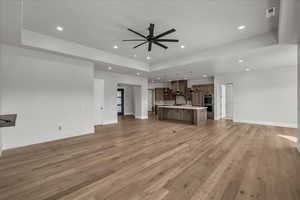 Unfurnished living room featuring a tray ceiling, light wood-style flooring, a ceiling fan, and recessed lighting