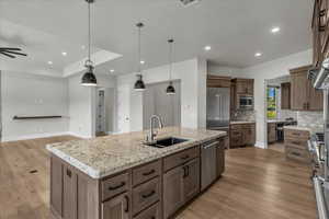 Kitchen with hanging light fixtures, a kitchen island with sink, light wood-type flooring, light stone counters, and recessed lighting