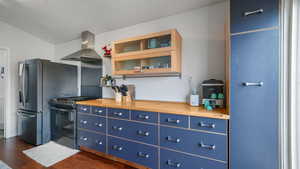 Kitchen featuring blue cabinetry, range with gas stovetop, wood counters, range hood, and dark wood-style flooring