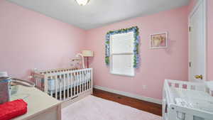 Bedroom featuring a crib and dark wood-type flooring