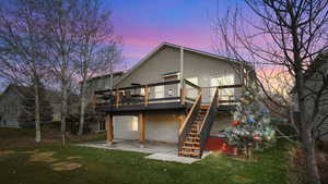 Back of house at dusk with a patio area, a deck, a yard, and stairs