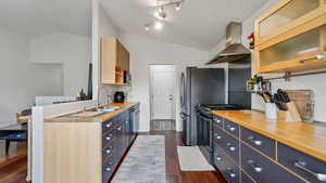 Kitchen featuring butcher block countertops, gas range, range hood, lofted ceiling, and dark wood-style flooring