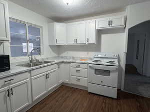 Kitchen featuring electric range, white cabinets, a textured ceiling, light countertops, and dark wood-type flooring