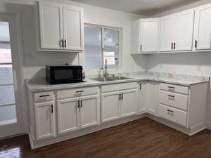 Kitchen with white cabinets, light countertops, black microwave, dark wood-type flooring, and a textured ceiling