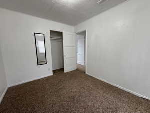 Bedroom with a textured ceiling, dark colored carpet, and a closet