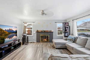 Living area featuring a textured ceiling, ceiling fan, wood finished floors, and a fireplace