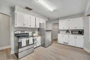 Kitchen with arched walkways, appliances with stainless steel finishes, white cabinets, and light countertops