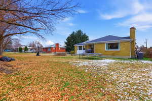 Rear view of property featuring a trampoline, brick siding, a chimney, and a lawn