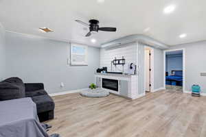 Living area with light wood-style flooring, ceiling fan, and a glass covered fireplace