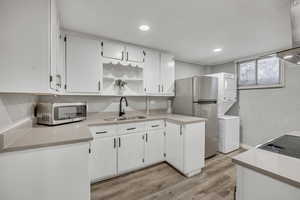 Kitchen featuring open shelves, white cabinetry, appliances with stainless steel finishes, light wood-style flooring, and extractor fan