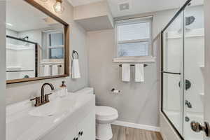 Bathroom with vanity, combined bath / shower with glass door, and light wood-style flooring