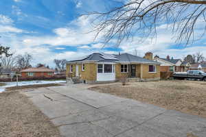 View of front facade featuring brick siding, roof mounted solar panels, driveway, and a chimney