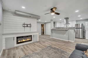 Living area with light wood-type flooring, stacked washing machine and dryer, recessed lighting, ceiling fan, and a glass covered fireplace