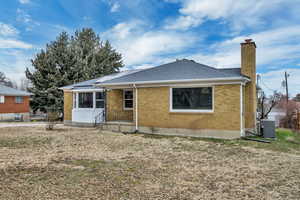 Back of property featuring a chimney, brick siding, roof with shingles, and roof mounted solar panels