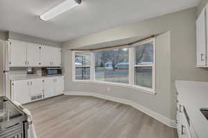 Kitchen featuring white cabinets, stainless steel appliances, light countertops, and light wood-style flooring