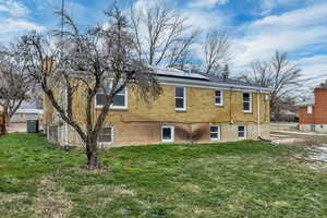 Back of property featuring roof mounted solar panels, brick siding, and a yard