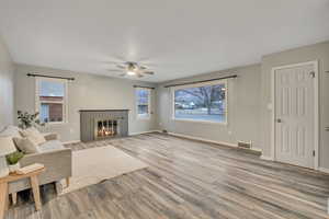 Living area featuring a fireplace with flush hearth, light wood-style floors, and ceiling fan