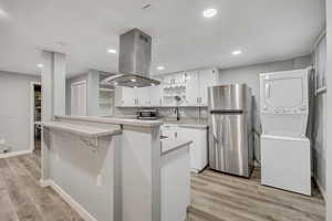 Kitchen with white cabinetry, light countertops, appliances with stainless steel finishes, a kitchen bar, and island exhaust hood