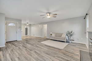 Living room featuring a ceiling fan, a brick fireplace, light wood-style floors, and arched walkways