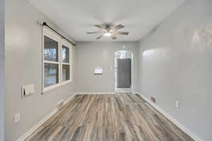Unfurnished room featuring arched walkways, light wood finished floors, and ceiling fan