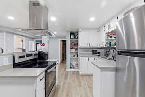 Kitchen featuring appliances with stainless steel finishes, open shelves, island exhaust hood, white cabinetry, and light wood finished floors