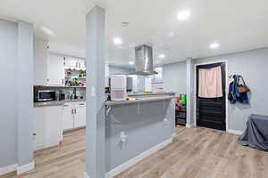 Kitchen featuring a kitchen bar, island range hood, white cabinetry, light countertops, and light wood-style flooring